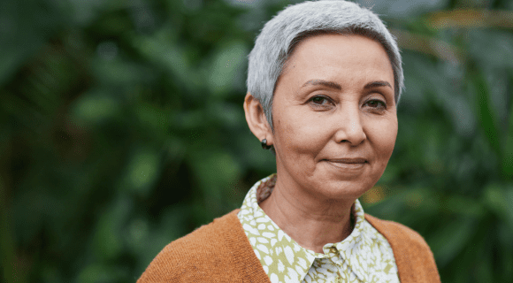 A smiling mature woman with short grey hair and an orange cardigan.