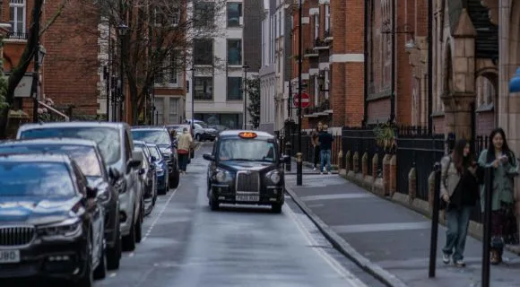 A black taxi driving near parked cars