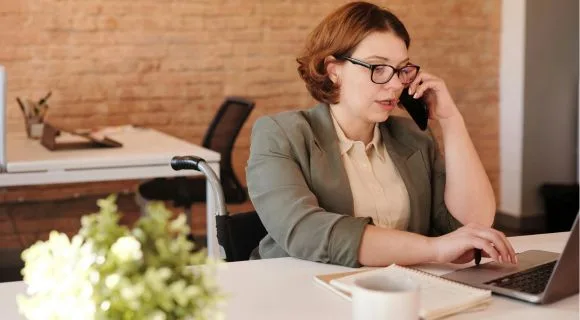 A woman on the phone, while typing on her laptop