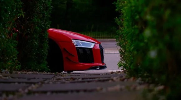 The hood of a red sports car between two hedges