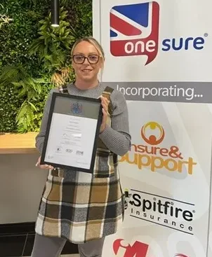 Nicole McGlade with her CII diploma in front of the One Sure Insurance logo.