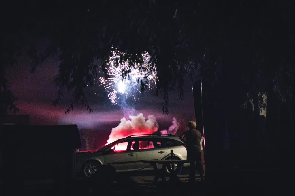 A car parked in the dark with fireworks exploding in the distance.