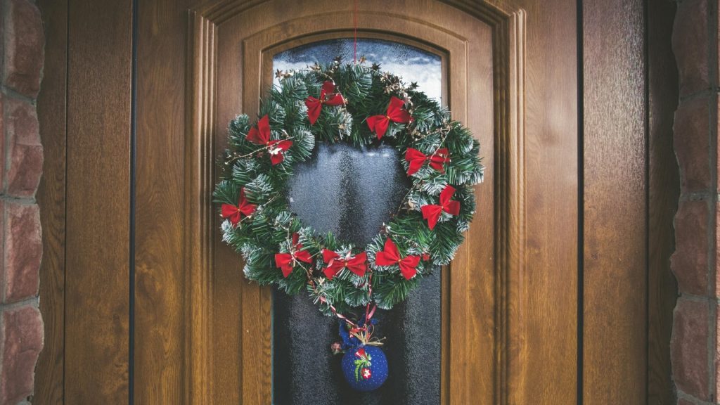 A wooden front door decorated with a Christmas wreath and red ribbons. 